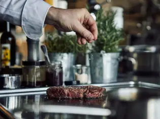 Eine Hand streut Salz auf ein Stück Fleisch.