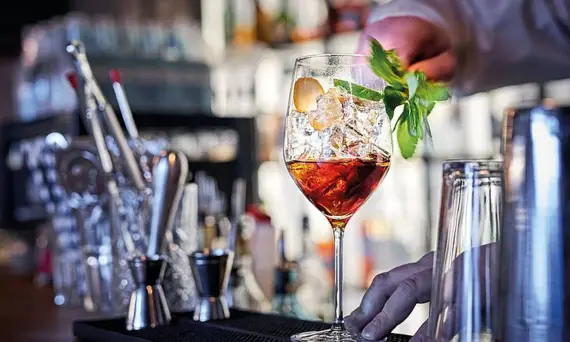 A Negroni on ice in a cocktail glass on a stem decorated with fresh mint on a bar counter.