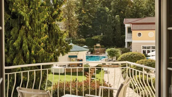 View from a balcony of a pool surrounded by trees and a building.