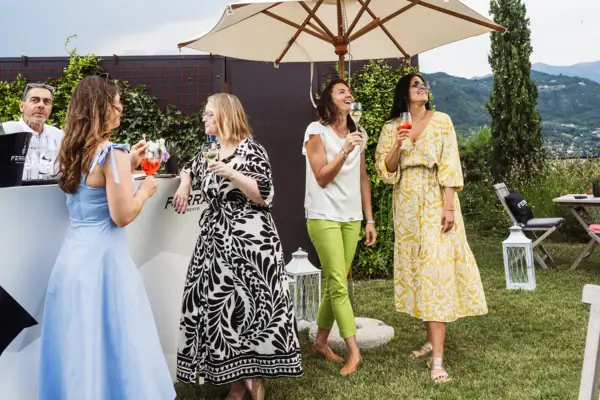 Gäste beim Empfang im Garten des A-ROSA Gardasee Gruppe von Gästen mit Getränken beim entspannten Empfang im Garten unter Sonnenschirmen.