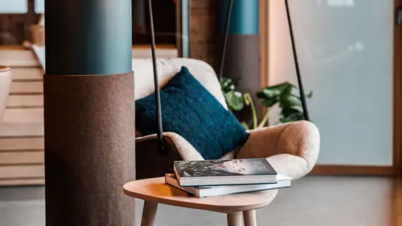 A swinging armchair with a dark cushion hangs next to a pillar. A side table with two books can be seen in the foreground.