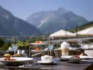 Outdoor table with dishes, including plates with food and drinks with mountains in the background.