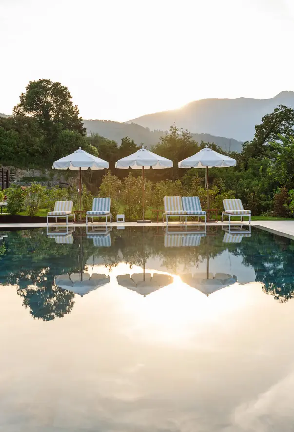 A pool with striped loungers and a green landscape in the background 