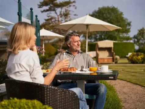 A man and a woman are sitting at a laid breakfast table outside.