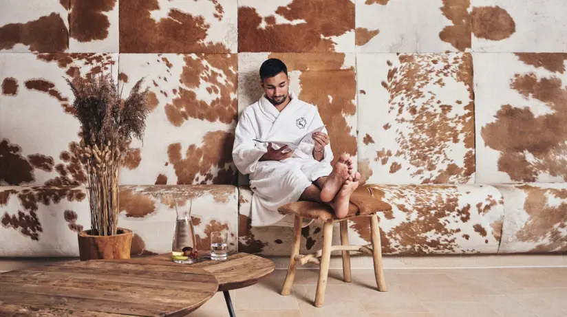 Man sitting on a chair with his feet crossed in front of a wall decorated with brown and white cowhide.