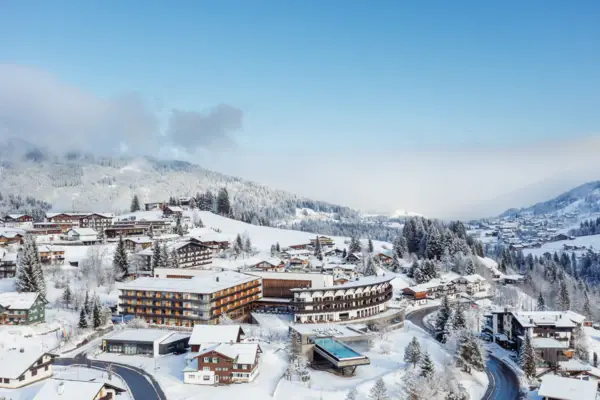 Building with a pool in the middle of a mountain village, surrounded by trees and a landscape with mountains.