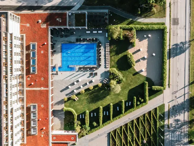 A swimming pool adjacent to a modern building, surrounded by trees and a well-maintained grassy area.