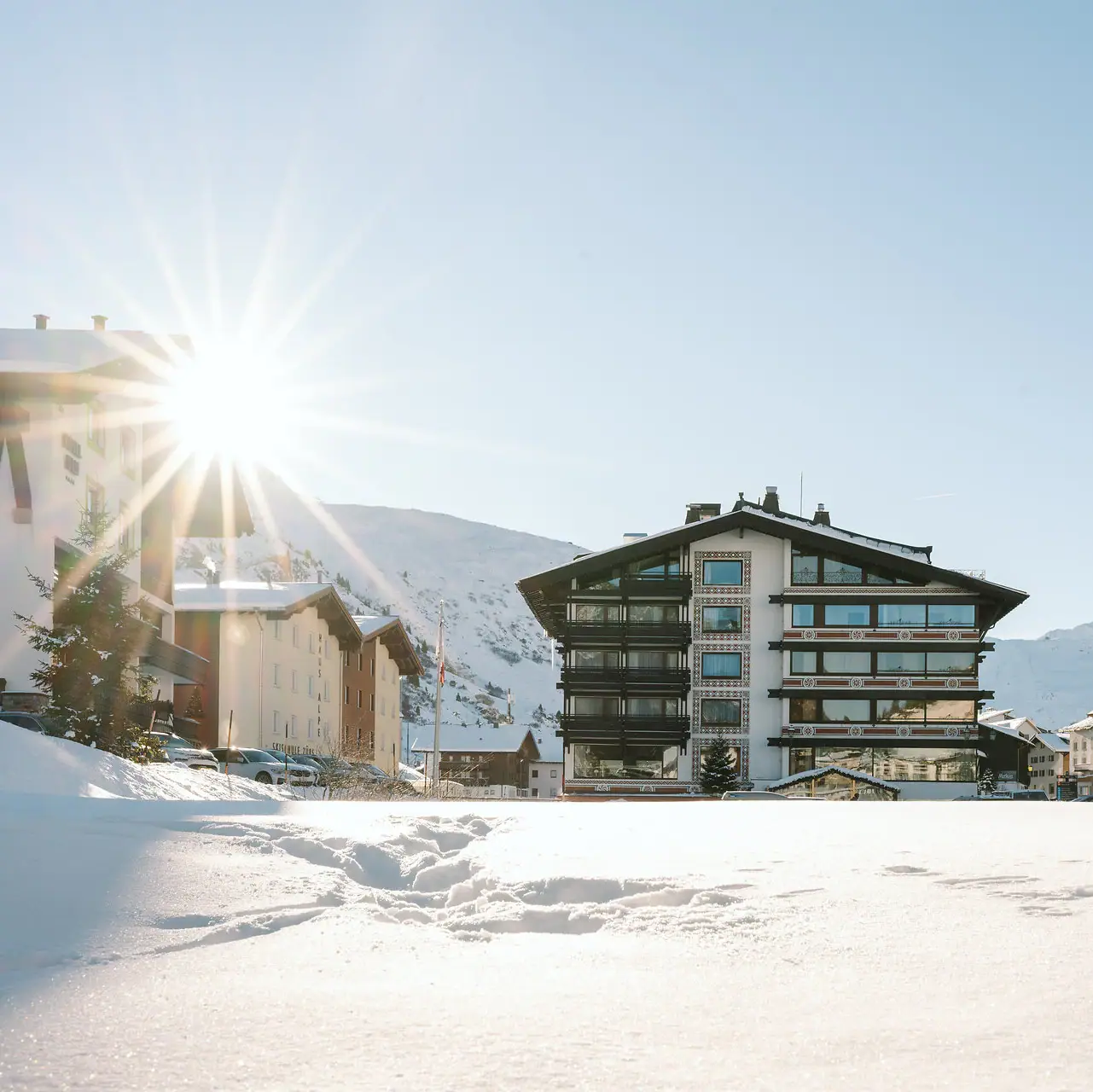 Schneebedeckter Boden mit Gebäuden und Bergen im Hintergrund.