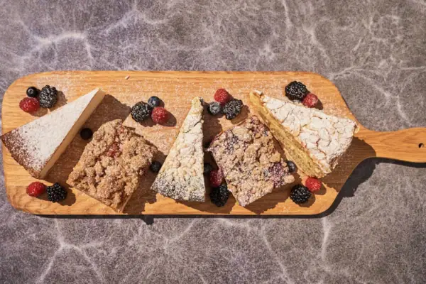 A wooden cutting board with various desserts, including fruit and baked goods.