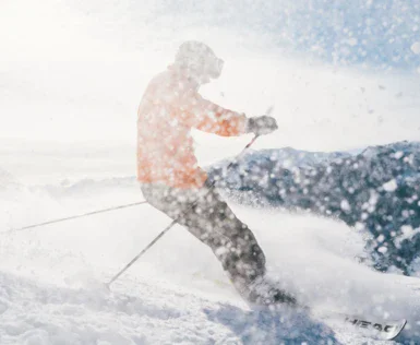 A skier stirs up the snow on a piste. the sun shines brightly on the cool white of the snow. 