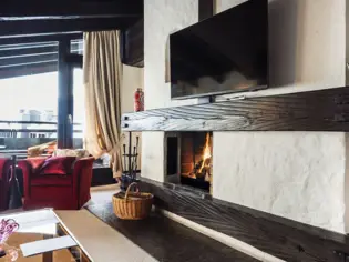 A cozy indoor setting featuring a fireplace with a TV mounted above it, surrounded by stylish furniture including a coffee table.