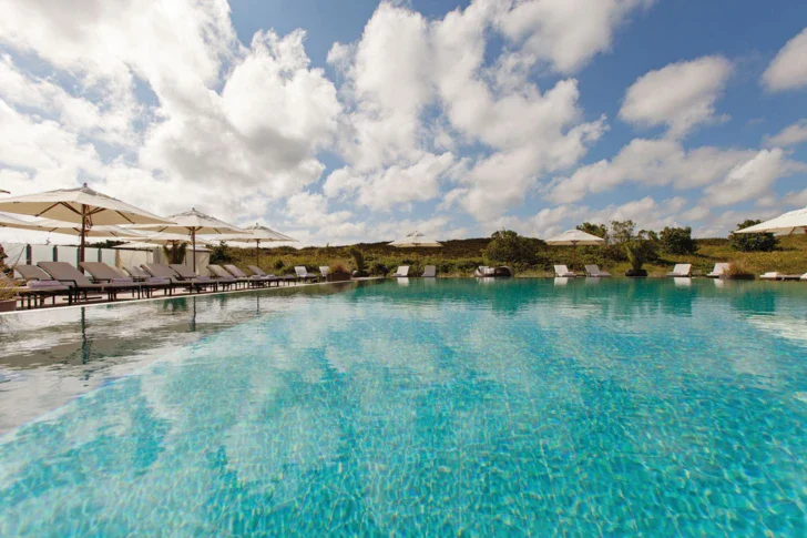 An elegant outdoor swimming pool surrounded by chairs and umbrellas under a cloudy sky.