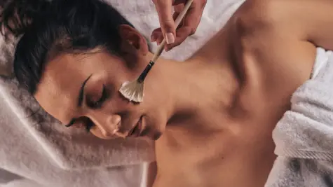 Woman lies inside and receives a facial treatment with a brush.