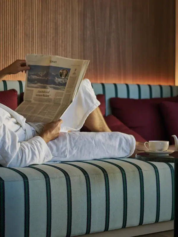 A man in a bathrobe reads a newspaper on a sofa.