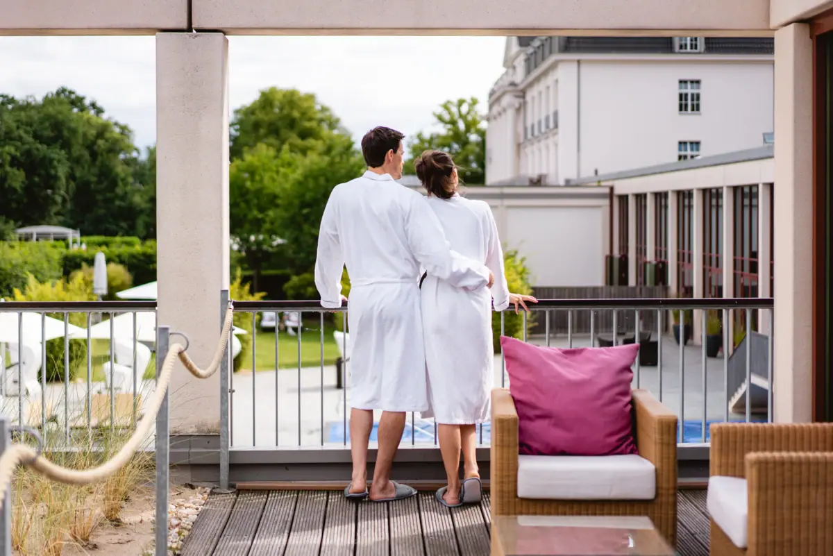 A man and a woman in white bathrobes are standing on a balcony.