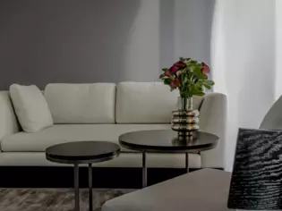 A seating area consisting of two light gray sofas and two small round tables with a flower vase. 