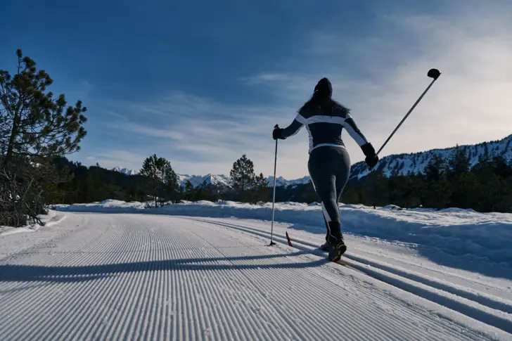 Cross-country skier on a snow-covered road in front of a mountain backdrop.