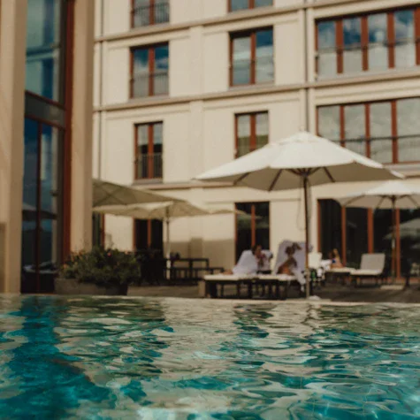 A wimming pool with umbrellas in front of a resort building.