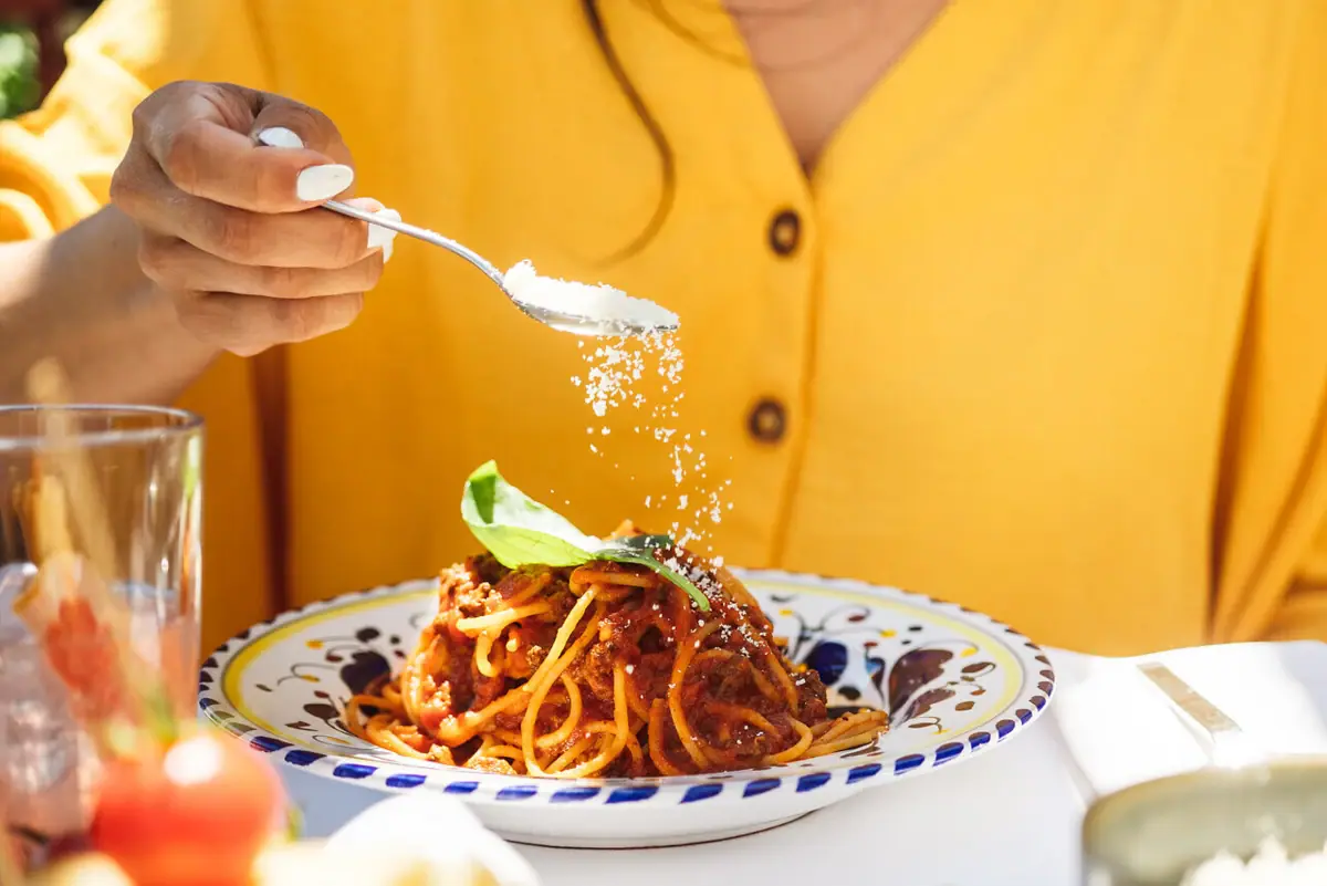 Restaurant at A-ROSA Lake Garda A person is sprinkling Parmesan over a plate of spaghetti.