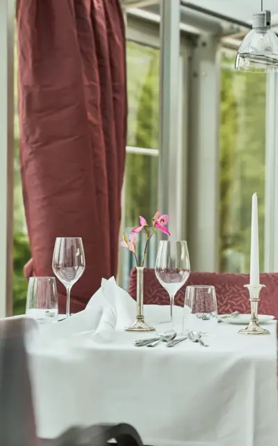 Elegantly laid table in a restaurant with tablecloth, crockery, wine glasses and a flower arrangement.