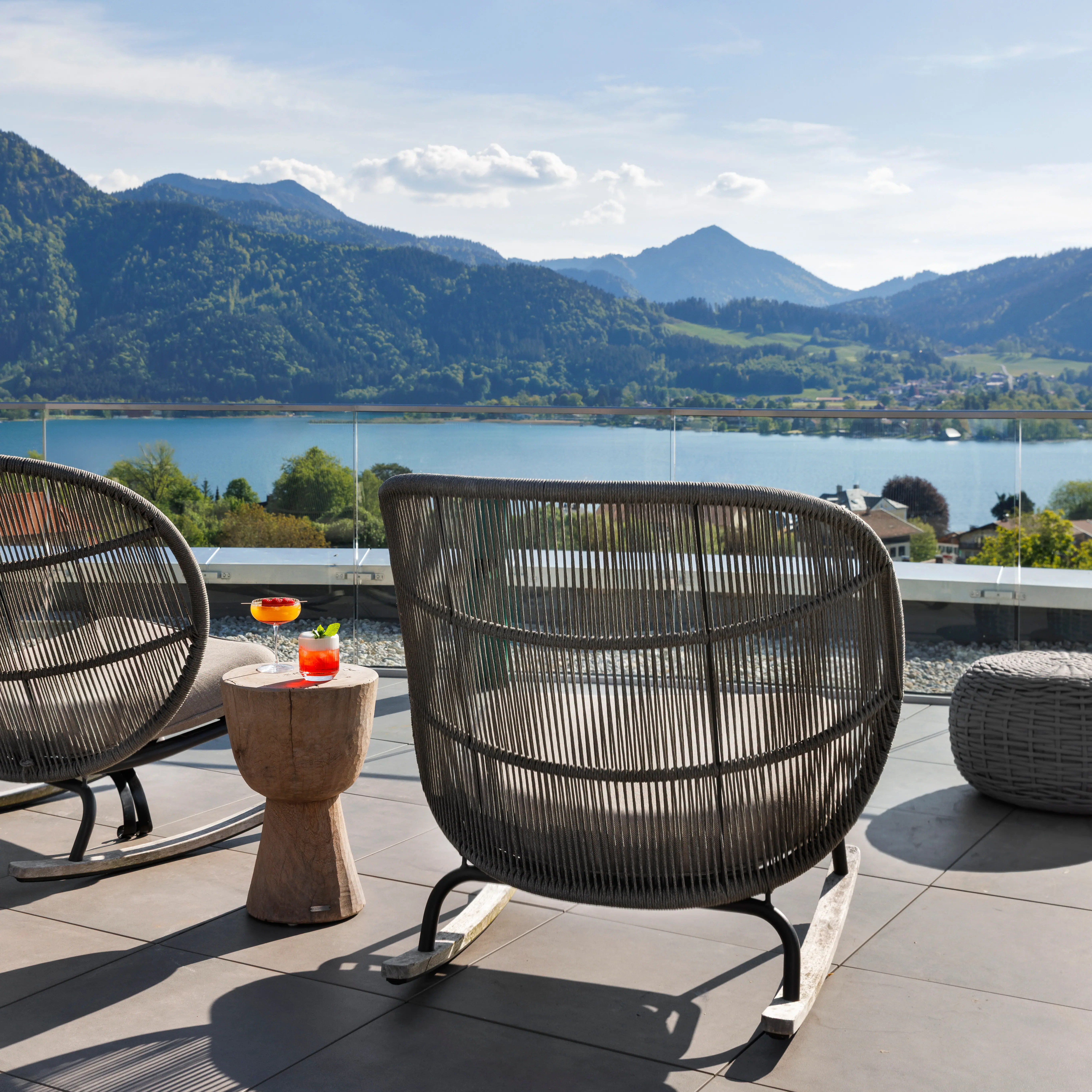 The terrace of the A-ROSA Tegernsee with armchairs and drinks and a spectacular view of Lake Tegernsee and the mountains.