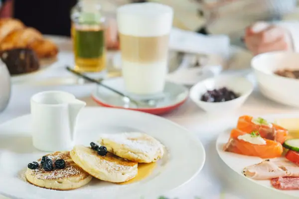 A plate of pancakes, garnished with blueberries and icing sugar.