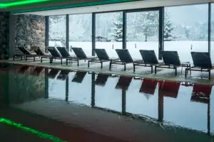 A swimming pool with chairs in front of a large window.