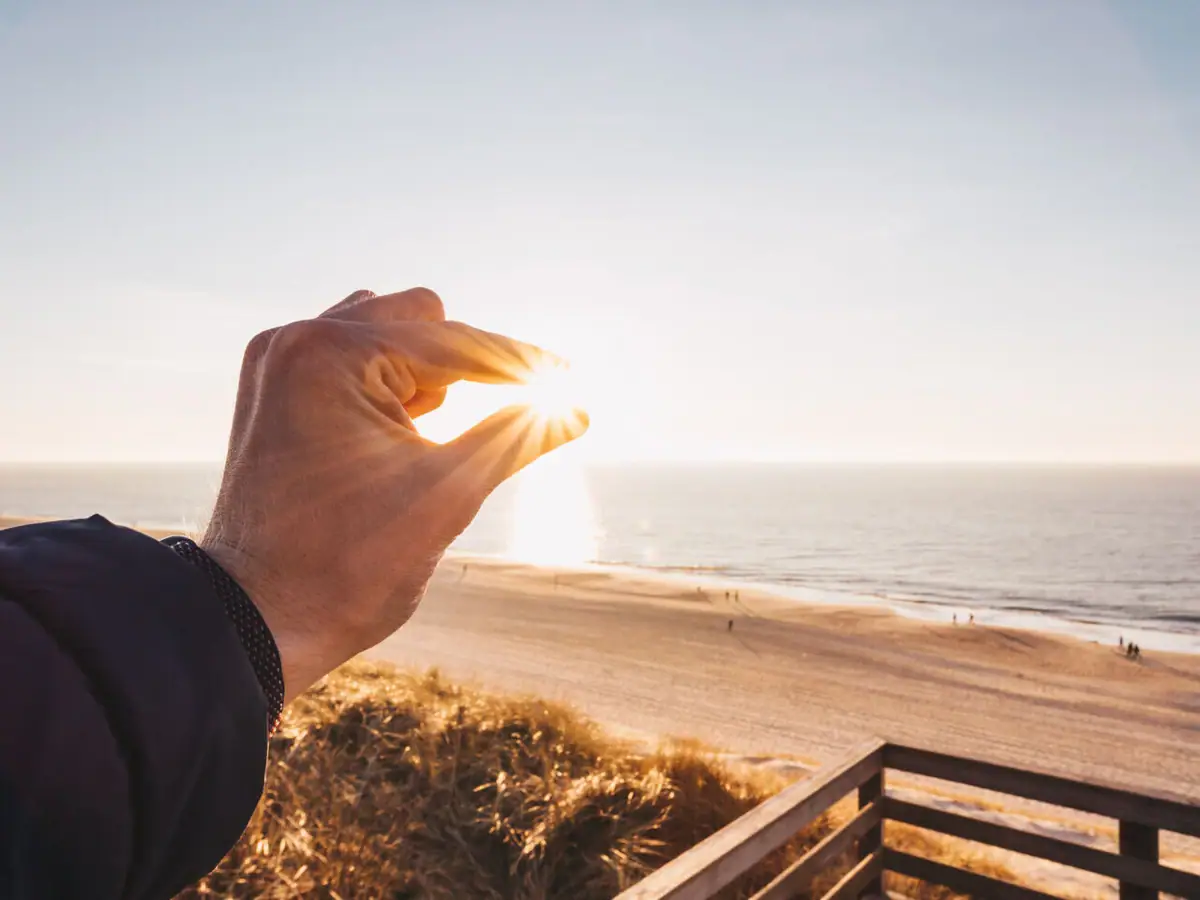 Hand hält die Sonne über einem Strand.