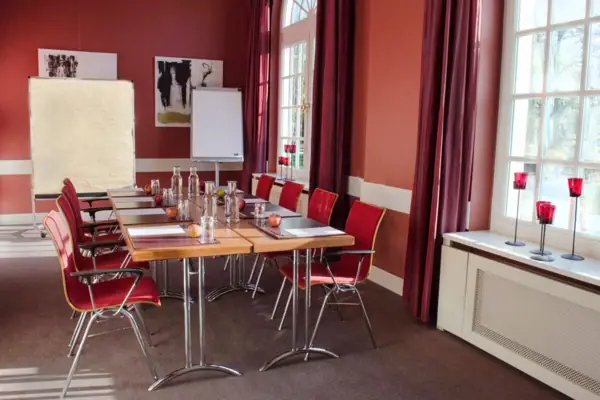 Veranstaltungsraum Passatzimmer Ein roter Veranstaltungsraum mit einem Tisch und Stühlen.