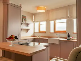 A bright kitchen with a kitchen island, to which a small counter is attached and three bar stools.