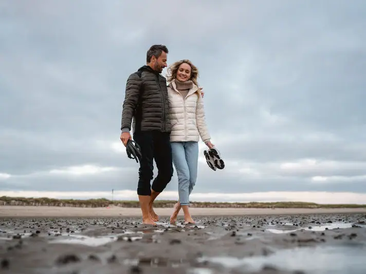Ein Mann und eine Frau gehen an einem nassen Strand entlang.