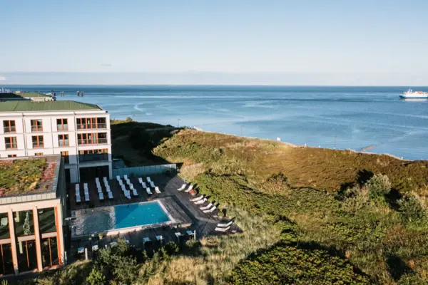 An outdoor pool in front of a building with a view of the sea in the background.