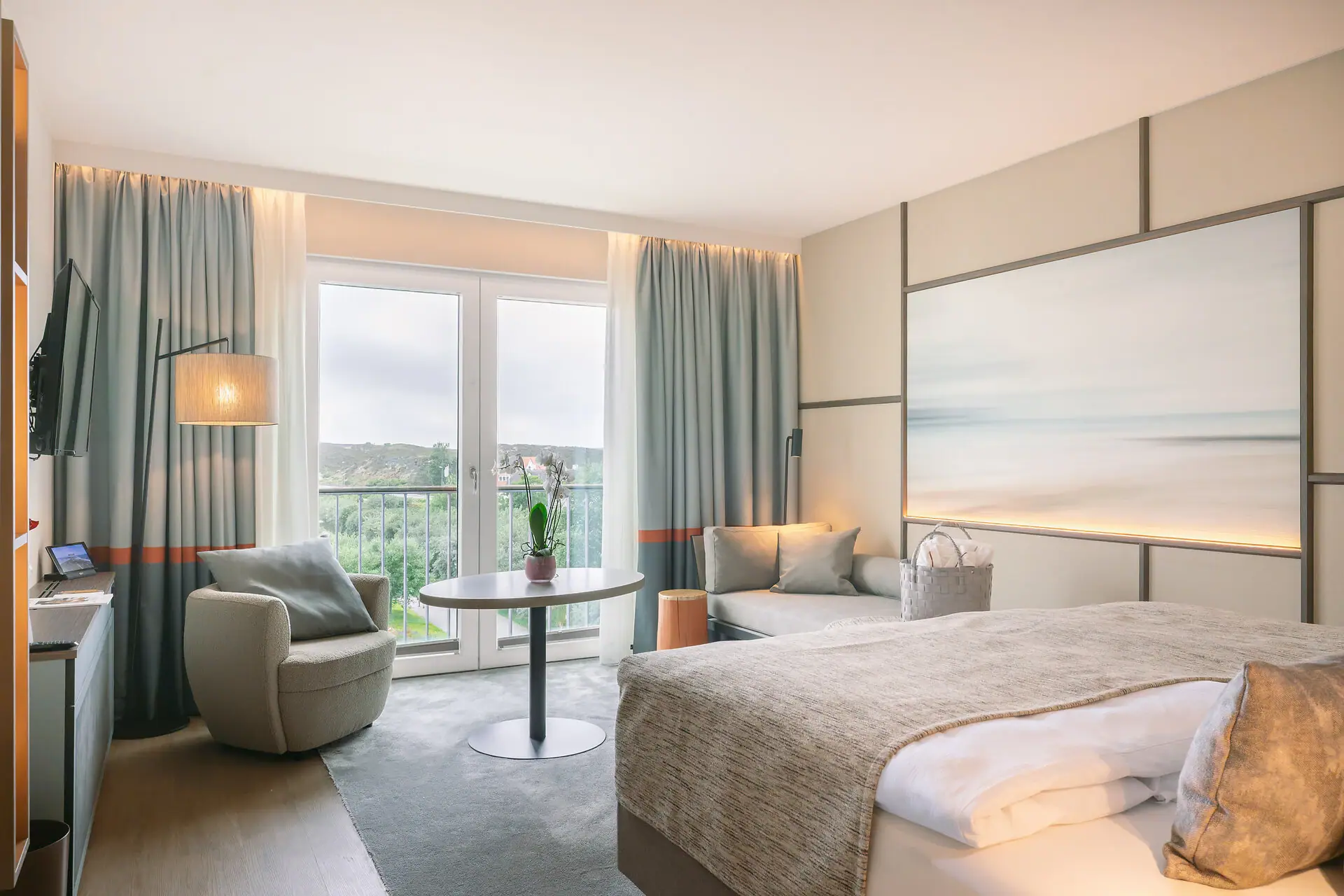 Zimmer Sylt Ein hochwertiges Hotelzimmer mit einem Bett, einem Tisch sowie einer Sitzecke und einem Sessel.