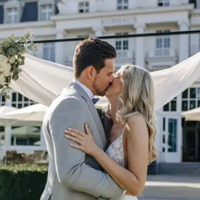 Ein Mann und eine Frau küssen sich im Freien, die Frau trägt ein Hochzeitskleid.