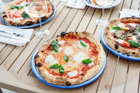 Several plates with pizza and wine glasses on a wooden table.