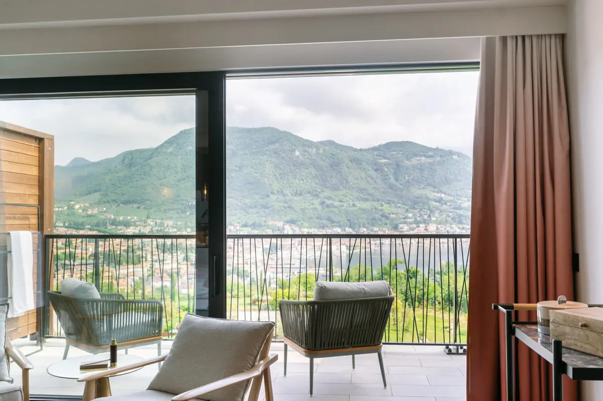 Rooms at A-ROSA Lake Garda A room with a balcony and a view of the mountains and trees.