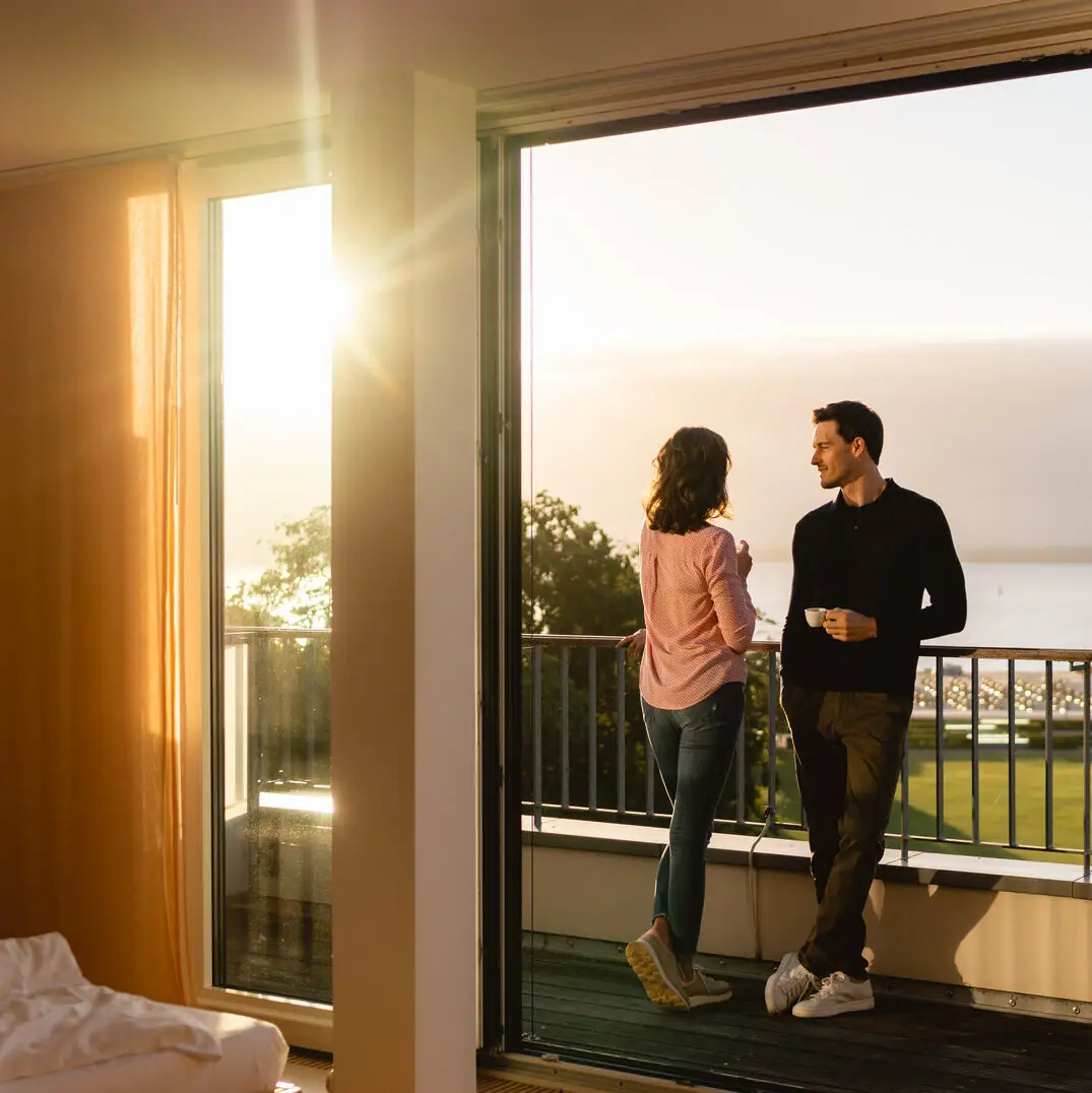 Ein Mann und eine Frau stehen auf einem Balkon und schauen aus einem Fenster.