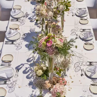 Ein für eine Dinnerparty oder Hochzeit gedeckter Tisch mit Tischwäsche, Geschirr und Blumenvasen als Mittelstück.