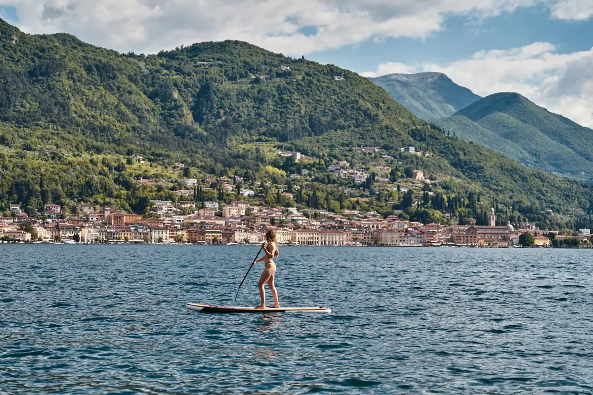 Stand-up paddleboarding on Lake Garda A woman on a paddleboard in the water, with a town in the background.