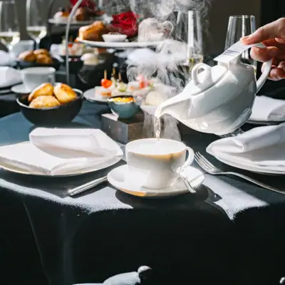 A person pouring tea into a cup on a table with tableware.