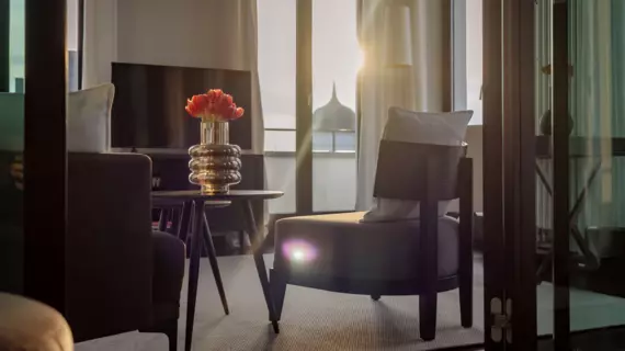 The living area of a suite can be viewed through a glass door. Comfortable armchairs, a table with red tulips and a television adorn this room. 