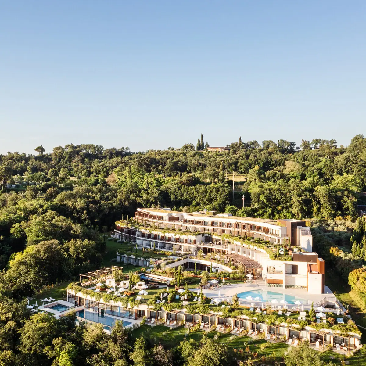 Luftaufnahme des A-ROSA Gardasee Hotels, eingebettet in grüne Hügellandschaft mit Poolanlage und Panoramablick auf den See.