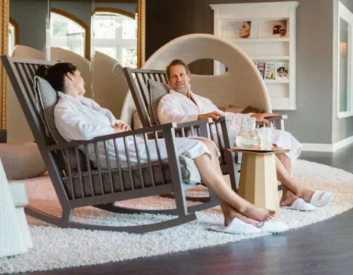 A man and a woman in white bathrobes are sitting in rocking chairs.