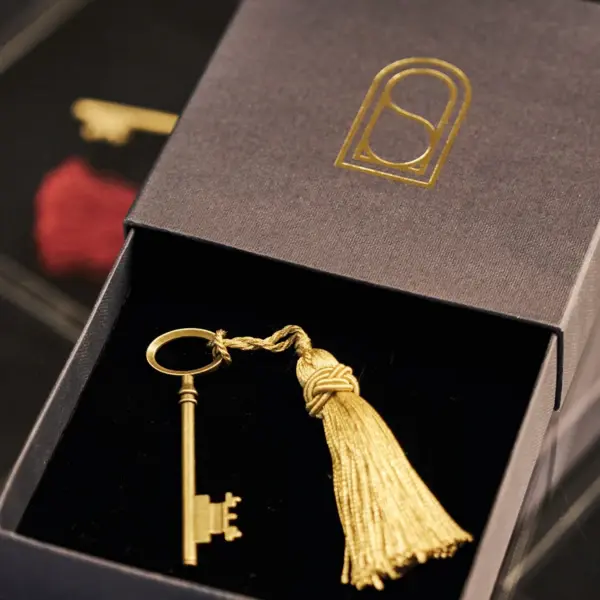 In a small square box lies a golden key with a golden pendant.