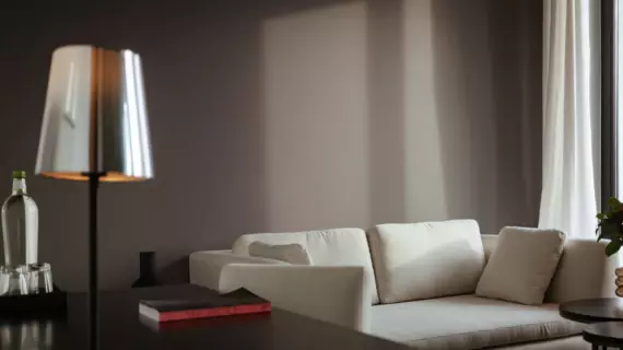 A light-colored sofa in front of a dark gray wall and a table in front of it with a small book on it. 