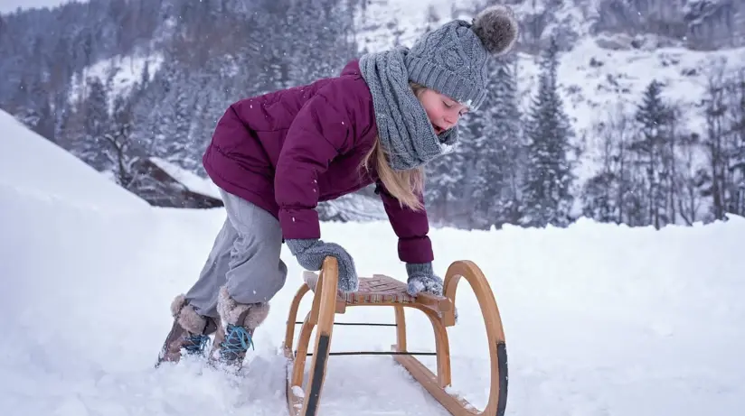 A girl in a purple jacket is leaning with her arms on a sledge standing in the snow.