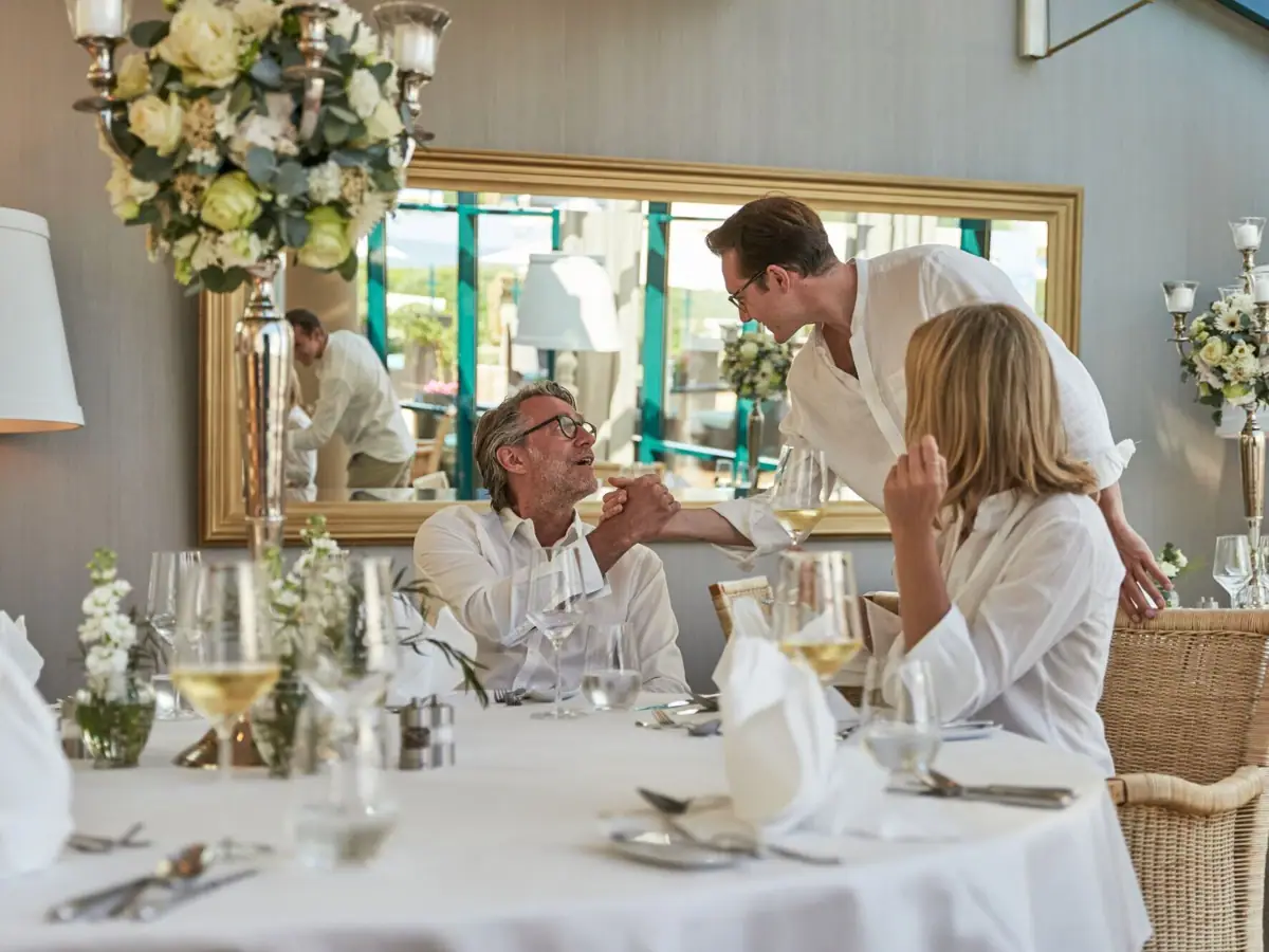 A group of people seated at a table with floral arrangements and tableware.