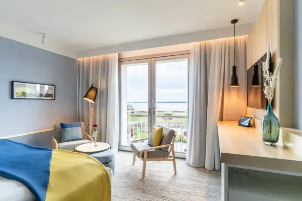 Zimmer A-ROSA Travemünde Hotelzimmer mit Bett, Tisch und Stühlen sowie einem großen Fenster mit Blick auf die Ostsee.