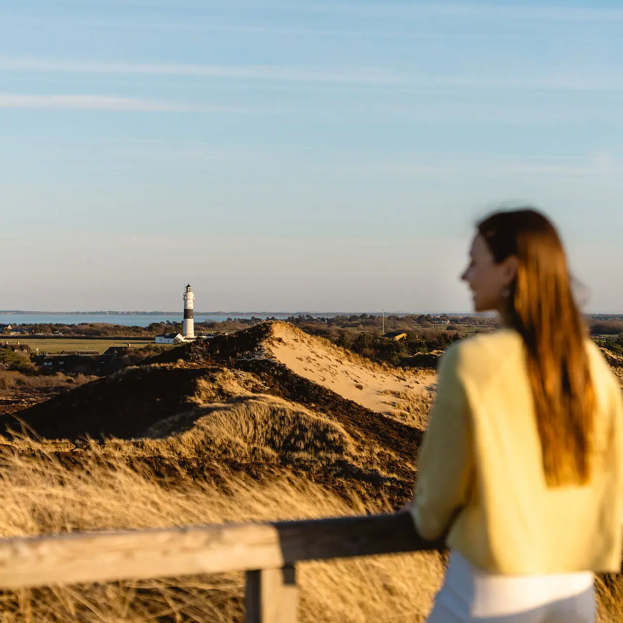 A woman is standing on a fence, looking towards a lighthouse on Sylt.