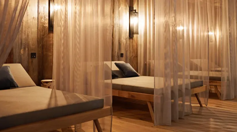 A warmly lid relaxation area with lounge beds separated from one another by transparent curtains. 